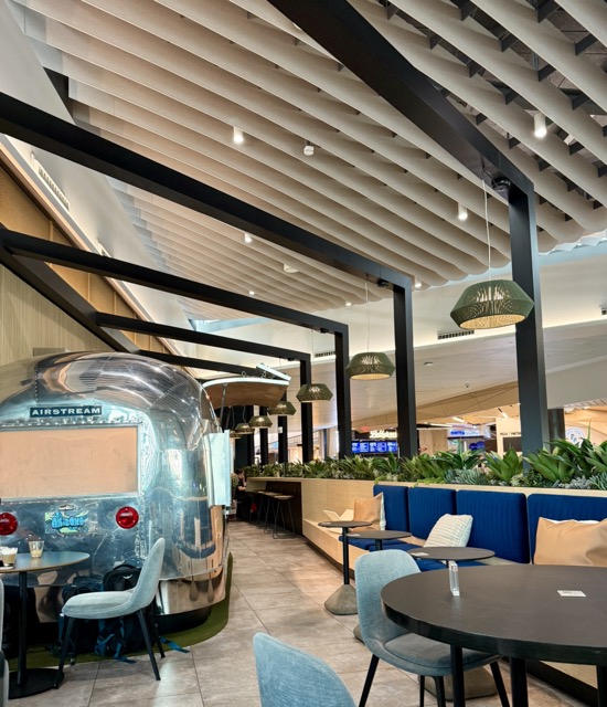 Interior del Chase Sapphire Lounge en Phoenix con áreas de descanso, mesas y un remolque Airstream convertido en estación de alimentos y bebidas.